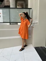 Vestido camisero de lino fucsia, de manga corta, con botones de nácar y un volado en el ruedo final. Además, cuenta con un volado superior en un solo lado, creando un efecto irregular y con diseño.