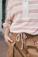 Remera tipo polo de tejido de punto a rayas horizontales en tonos rosados y beige. Presenta cuello camisero de lino, cierre frontal con botones de nácar y silueta holgada.