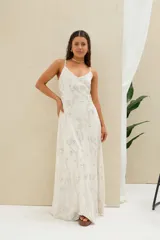 Vestido largo de lino beige con tirantes finos y escote en V, adornado con sutiles bordados florales plateados y lentejuelas.