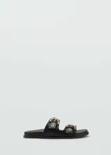 Sandalias planas de color negro con dos tiras en el empeine, cada una decorada con una hebilla metálica dorada y ojales.