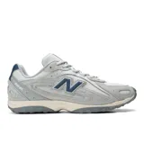 Championes New Balance modelo 204L, con diseño inspirado en el running de los años 2000. Presenta una capellada de ante y malla en tonos grises, con detalles en azul marino en el logo lateral y el talón. Cuenta con una suela de EVA con diseño técnico y líneas arqueadas.
