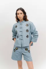 Chaqueta liviana de jean celeste con cuello mao, cierre frontal con alamares y detalle de bordados florales.
