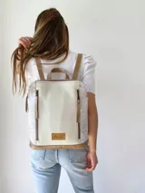 Mochila de cuero color beige y blanco, con detalles laterales texturizados, bolsillos frontales verticales con cierre y asas ajustables.