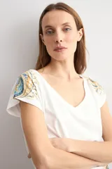 Remera blanca de manga corta, con escote en V y detalles de estampa paisley en los hombros y en el borde inferior.