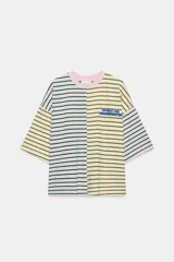 Camiseta oversize con diseño bicolor a rayas horizontales, combinando un lado en tonos rosado y verde oscuro, y el otro en beige y marrón. Cuenta con cuello redondo, mangas cortas amplias y texto bordado en azul en el pecho.