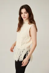 Chaleco de punto sin mangas con cuello polera, diseño de trenzas y rombos en relieve, y detalle de flecos largos en el ruedo.