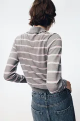Polo de punto fino confeccionado en lana, con diseño de rayas horizontales en tonos gris, blanco y rosado. Presenta cuello polo, manga larga y cierre frontal con botones.