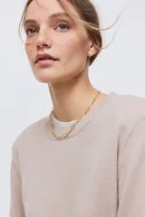 Buzo en punto fino suave de color beige con hombreras y ribete acanalado en cuello redondo, puños y bajo.
