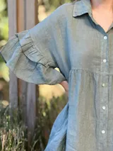 Vestido camisero blanco de lino italiano, con cuello camisero, cierre frontal con botones, mangas cortas con doble volado y bolsillos laterales.