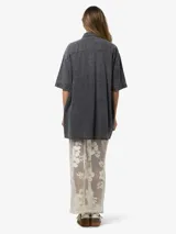 Vestido camisero corto de denim negro con lavado ácido, manga corta, cierre frontal con botones, dos bolsillos con solapa en el pecho y corte holgado.