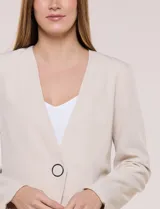Blazer de sastrería color beige, sin solapas, con cuello en V profundo y cierre frontal de un único botón circular metálico en contraste.