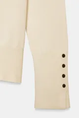 Jersey de punto liso color negro, con cuello redondo y manga larga. Presenta una hilera de cuatro botones dorados decorativos en el puño de cada manga.