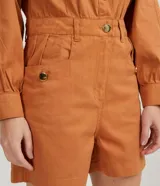 Mono corto color ladrillo, de sarga de algodón, con cuello mao, mangas abullonadas largas, cierre frontal con botones dorados, bolsillos laterales y cintura marcada.