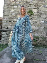 Vestido midi de corte holgado con estampado tipo paisley en tonos azul y blanco. Presenta mangas tres cuartos, escote redondo con pequeña abertura frontal y cordón ajustable en la cintura con borlas decorativas.