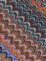 Chal o bufanda de punto con patrón zigzag multicolor, característico de Missoni, con flecos en los extremos. El tejido combina tonos tierra, naranjas, morados y fucsias.