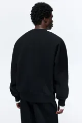 Buzo negro de tejido liviano con mezcla de algodón y viscosa, manga raglán y cuello redondo. Puños y bajo acanalados. Corte oversized para una silueta holgada.