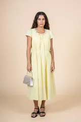 Vestido midi de color amarillo claro, con escote redondo adornado con pequeñas cuentas decorativas, mangas cortas y falda con caída fluida. Incluye un lazo ajustable en la cintura para entallar la silueta.