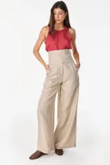 Pantalón de lino blanco de corte ancho y fluido, con cintura alta que incorpora una sobrepretina ancha desmontable con pliegues horizontales.