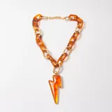 Collar de cadena gruesa con eslabones alternados de resina color ámbar y metal dorado, con dije central en forma de rayo de resina color naranja.