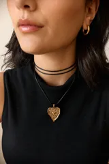 Collar con dije de corazón en acero quirúrgico, con textura irregular y relieve, montado sobre un tiento encerado negro.