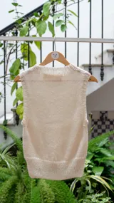 Chaleco tejido de punto en color crudo, con cuello alto y diseño sin mangas. Presenta una textura de punto grueso y corte recto.