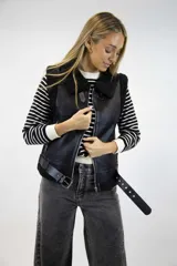 Chaleco gamulán de cuero sintético color marrón oscuro con interior y solapas de corderito negro. Cuenta con cierre frontal metálico, bolsillos laterales con cierre y tiras con hebilla ajustable en el bajo y el cuello.