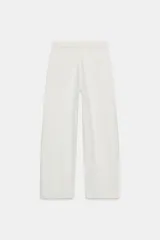 Jeans de mezclilla azul claro, tiro bajo, con corte ancho y pierna recta. Presenta un detalle de cintura cruzada o vuelta con un nudo o pliegue frontal y un ligero desgaste en una de las piernas.