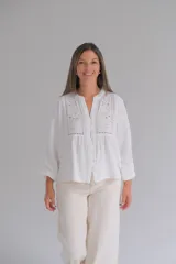 Blusa blanca de manga larga con cuello mao y cierre frontal con botones. Presenta detalles de bordado inglés y calados en la parte superior delantera.
