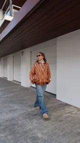 Buzo tipo saco abotonado con diseño de cuadros en tonos marrones y beige, corte recto y oversize. Presenta cuello camisero, cierre frontal con botones personalizados y dos bolsillos delanteros.
