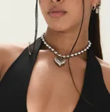 Collar tipo gargantilla plateado con eslabones de cuentas y dijes colgantes: un corazón plateado tridimensional y pequeños cristales incrustados entre las cuentas.