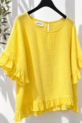 Blusa blanca de tela liviana y fresca, con mangas cortas abullonadas terminadas en volados y detalle de volado en el ruedo. Presenta escote redondo con pequeña abertura y botón en la parte posterior.