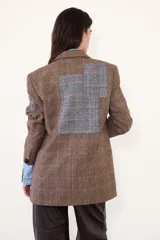 Blazer de corte sastrero confeccionado en paño con estampado de cuadros escoceses. Presenta parches decorativos en las mangas y espalda, bordados en el bolsillo y manga, y cierre frontal con botones.