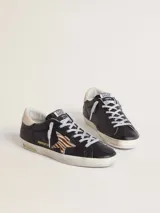 Zapatilla Golden Goose modelo Super-Star, confeccionada en cuero vacuno negro con efecto desgastado. Presenta la clásica estrella lateral de pelo con patrón animal print tipo cebra, contrafuerte en cuero nude y cordones con hilo plateado. Suela de goma con acabado envejecido y detalles con inscripciones doradas.