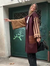 Sacon de diseño asimétrico en tonos bordó y marrón, con una manga lisa y otra a rayas horizontales. Presenta bolsillos frontales con apliques de cuero sintético y corte largo abierto.