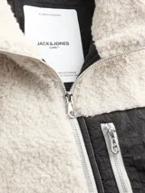 Campera de tejido tipo teddy color beige, con cuello alto y cierre frontal. Presenta un bolsillo frontal en contraste de color negro con cierre vertical y el logo de la marca estampado.