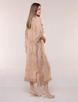 Vestido midi tipo túnica de silueta holgada, marca America & Beyond, color rosado con estampado metalizado dorado de palmeras. Cuenta con escote en V, detalles de borlas, espejos y apliques decorativos, y flecos en mangas, laterales y ruedo.