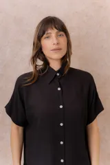 Camisa negra de calce amplio y relajado, confeccionada en tejido liviano con textura sutil. Cuenta con diseño oversize, hombros caídos, mangas cortas amplias, cuello camisero y abotonadura frontal con botones claros.