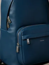 Mochila Calvin Klein de poliuretano texturizado en color azul, con compartimento principal con cierre de doble cremallera, bolsillo frontal con cierre, asa superior y tirantes ajustables. Incluye detalle de logo metálico de la marca en el frente.