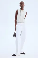 Chaleco corto de punto suave color blanco hueso, con cuello camisero y tapeta de tres botones oscuros. Presenta ribete acanalado en sisas y bajo.