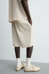 Bermuda de corte relajado, color crema o blanco roto, con textura acanalada (canalé). Presenta cintura elástica ajustable con cordón, bolsillos de vivo frontales y un bolsillo plastrón trasero.