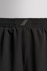 Pantalones cortos negros de tejido técnico perforado, ligeros y elásticos. Cuentan con cintura elástica ajustable con cordón interior, bolsillos frontales, bolsillo trasero de seguridad con cierre de cremallera, perneras con laterales perforados para transpirabilidad, bajo con acabado termofijado y aberturas laterales. Incluye detalle de logo estampado en la pernera.