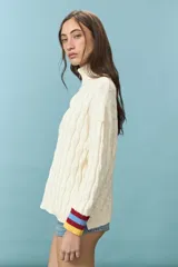 Sweater de tejido de punto con estructura de ochos en color natural, de cuello alto y manga larga. Presenta un bordado de sol en la espalda y puños con franjas de colores en rojo, celeste y amarillo.