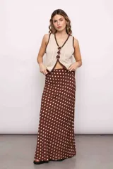 Chaleco tejido color crema con escote en V y ribete marrón. Presenta tres flores de crochet marrones a modo de cierre.