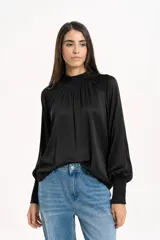 Blusa de satén color negro, con cuello alto fruncido y mangas largas abullonadas con puños elásticos.