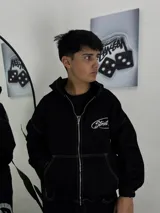 Campera de denim negro con capucha, cierre frontal de cremallera metálica y costuras visibles en color blanco. Presenta bolsillos frontales tipo canguro y detalle bordado o estampado con la palabra "Street" en el pecho.