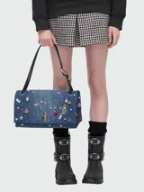 Cartera tipo shoulder bag de Marc Jacobs confeccionada en denim azul, decorada con múltiples charms metálicos y de cristal, incluyendo figuras de labios, cerezas, estrellas y dados. Cuenta con cierre frontal metálico y correas de hombro de cuero negro.