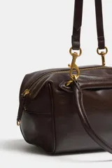 Bolso de hombro tipo bowling o mini shopper, color marrón oscuro, con doble asa superior y herrajes metálicos dorados. Presenta un diseño estructurado y compacto.