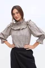 Blusa de algodón a rayas color beige, con cuello alto fruncido, volados en los hombros y mangas abullonadas con puños elásticos con volados.