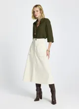 Falda midi color crudo, de tela tejida, con bolsillos delanteros, cierre frontal con cremallera y botón, y trabillas para cinturón.