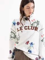 Buzo de silueta holgada y diseño rústico en color blanco, con estampado floral full print y la inscripción "LE CLUB" en el pecho. Cuenta con capucha, ojales metálicos y cordón regulable.